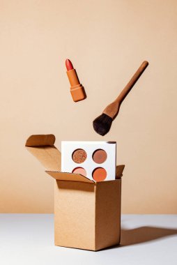 brown luxury lipstick and brush levitating over box and gainst a brown background clipart