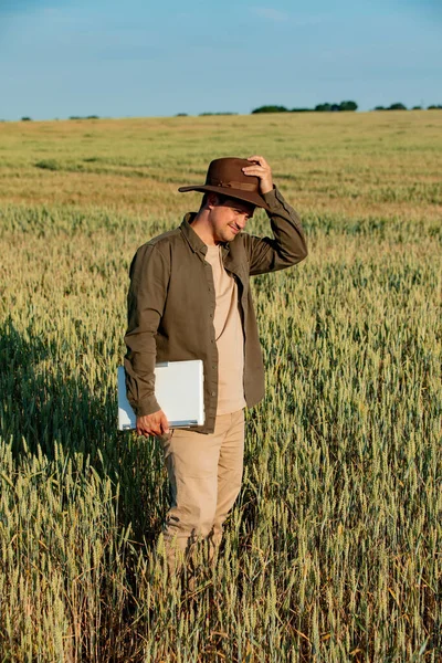 Farmer in hat with laptop computer on wheat field