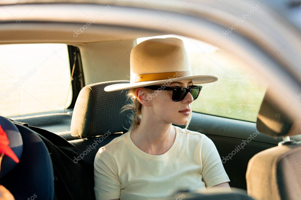 Stylish woman in hat sit as passenger in a car