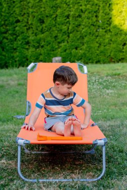 Küçük çocuk açık havada turuncu güneş yatağında oturuyor. 