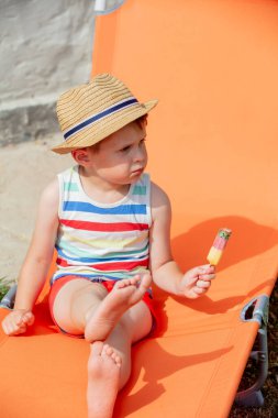 Küçük çocuk turuncu güneşli yatakta oturur ve dondurma yer.