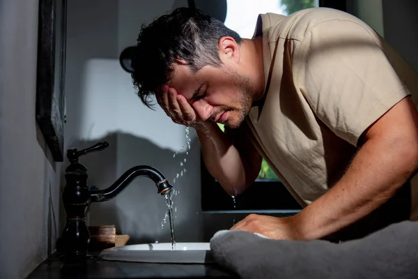 man washes his face in the bathroom in the morning