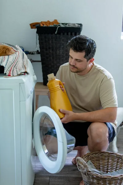man pours liquid laundry detergent into the washing machine at home