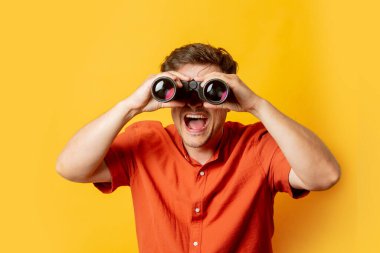 Dürbünlü turuncu gömlekli adam sarı arka planda.