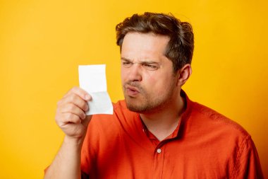 Şaşkın adam sarı arka plandaki kağıt sayfasına bakıyor.