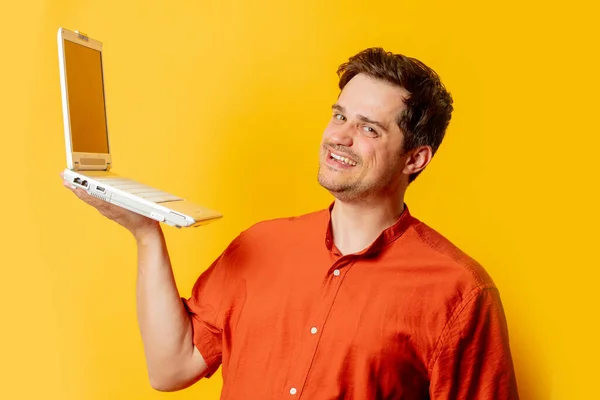 Stylish man in orange shirt with laptop computer on yellow background