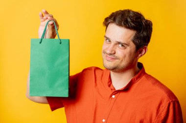 Sarı arka planda kağıt alışveriş torbası olan şık bir adam.