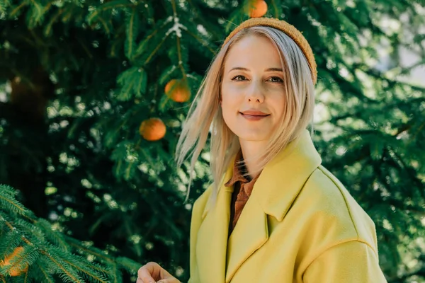 woman in yellow coat hangs oranges on the branches of the Christmas tree