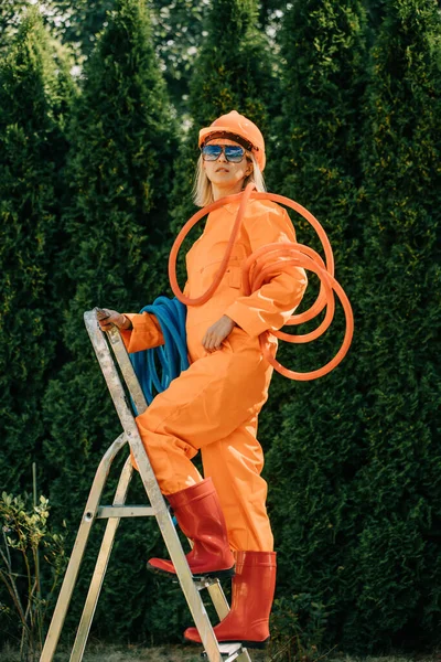 Stylish Woman Orange Suit Hardhat Pipes Sunglasses Next Stepladder Gray — Fotografia de Stock