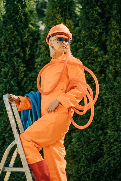Stylish Woman Orange Suit Hardhat Pipes Sunglasses Next Stepladder Gray — Fotografia de Stock