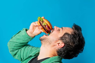 Mavi arka planda hamburgerli yeşil tişörtlü beyaz adam.