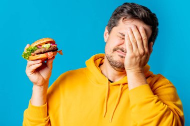 Sarı kapüşonlu beyaz adamın mavi arka planda hamburger yemesine şaşırdım.