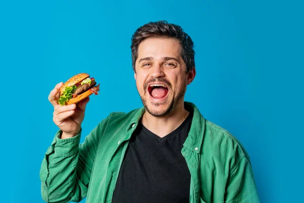Smiling white guy in green shirt with hamburger on blue background