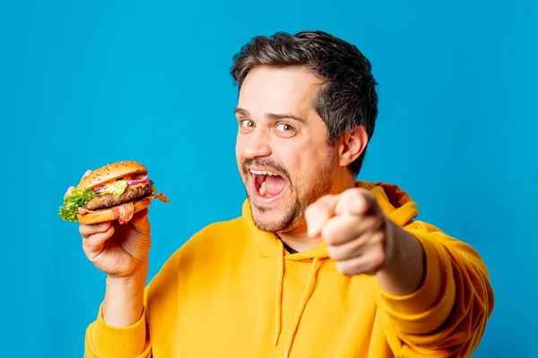 Šťastný Bílý Chlap Žluté Mikiny Jíst Hamburger Modrém Pozadí — Stock fotografie