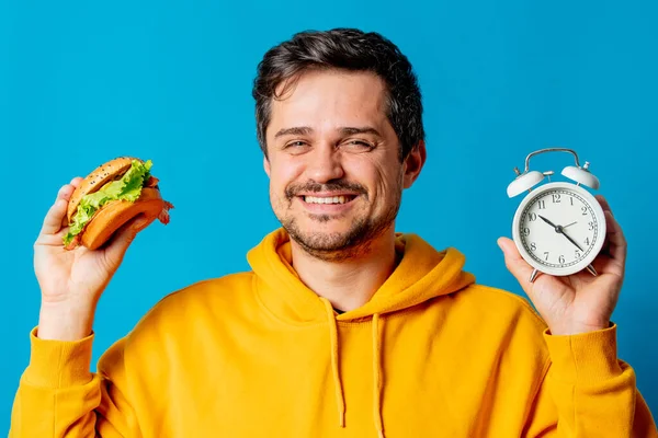 Bílý Chlap Žluté Mikině Hamburgerem Budíkem Modrém Pozadí — Stock fotografie