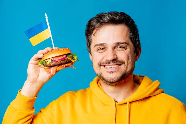 Bílý Chlap Žluté Mikině Hamburgerem Ukrajinskou Vlajkou Modrém Pozadí — Stock fotografie