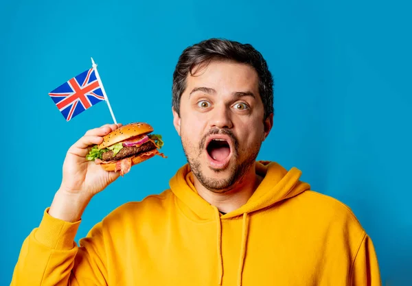 Usmívající Chlap Žluté Mikině Hamburgerem Vlajkou Velké Británie Modrém Pozadí — Stock fotografie