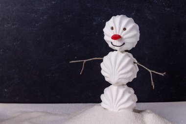 Beyaz şekerlemelerden ve marmelattan yapılmış bir kardan adam mavi bir zemin üzerinde granüllenmiş şeker yığınının içinde duruyor.