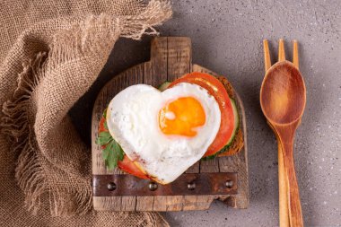 Sebzeli sandviç ve tahtanın üzerinde kalp şeklinde yumurta.