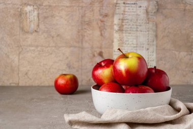 Kırmızı elmalar bej arka planda beyaz bir seramik kasede yatıyor.