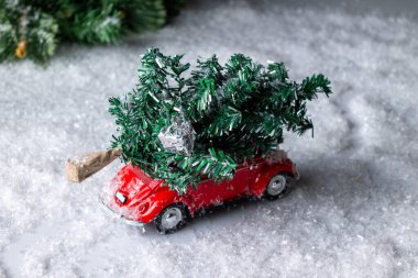 Çatıda bir ağaç olan kırmızı oyuncak araba karlı ormanda koşuyor.