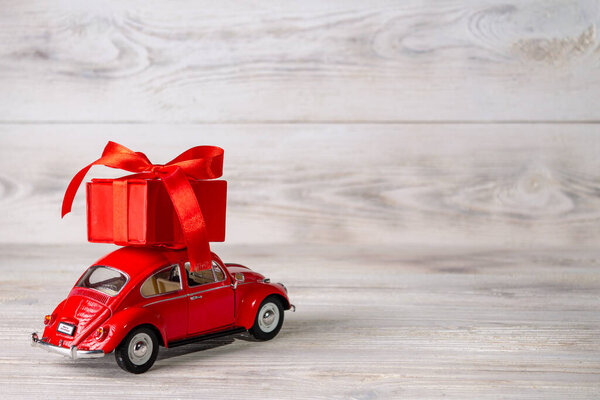 red car with a gift on the roof on a white wooden background, place for text