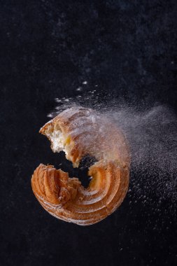 Kremalı çörek, siyah arka planda şeker tozunda uçuşuyor.