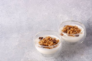 iki cam bardak müsli, yoğurt, gri arka planda çikolata.