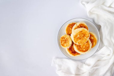 süzme peynirli kekler beyaz arkaplanda beyaz seramik bir tabakta, fotokopi alanı ile uzanıyorlar.