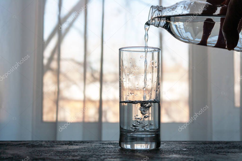 water pours from a bottle into a glass on the background of the window