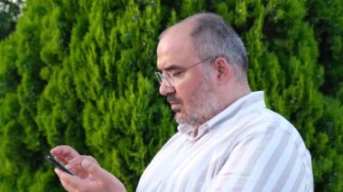 Telefonunu, cep telefonunu açık havada kullanan bir adam.