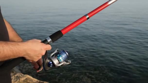 Carrete de pesca, un hombre gira el carrete de pesca junto al mar — Vídeos de Stock