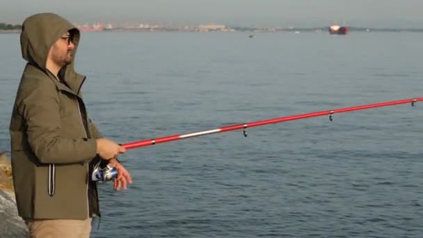 Joven pescador, joven está pescando con una caña de pescar junto al mar — Vídeo de stock