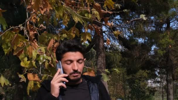 Telefonon beszél, fiatal férfi beszél telefonon a fák előtt, ősz — Stock videók