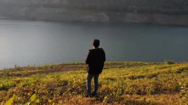Gölü izlerken, genç adam yeşil çayırların arasından özenle gölü izliyor.