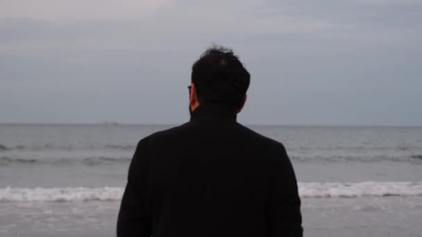 Один чоловік, один чоловік в пальто, спостерігаючи за морем з повернутою спиною — стокове відео