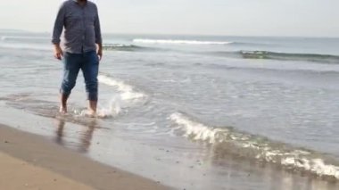 Denizde yürüyen, orta yaşlı bir adam sonbaharda sahilde yürür.