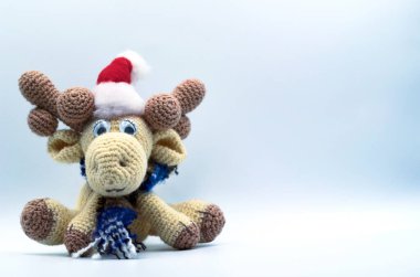 Oyuncak yeni yıl geyiği yünden örülmüş, oyuncak geyik kafasında Noel Baba şapkasıyla oturur, atkıda geyik, el yapımı yumuşak oyuncak, mesaj için yer
