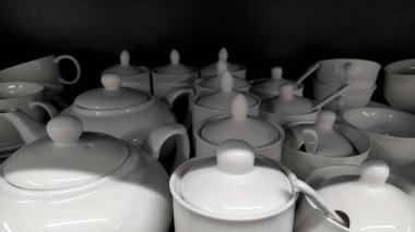 Beyaz tabaklı raflar, ev eşyaları mağazasında bulaşık sırası, beyaz servis, beyaz çaydanlık ve şeker kasesi.