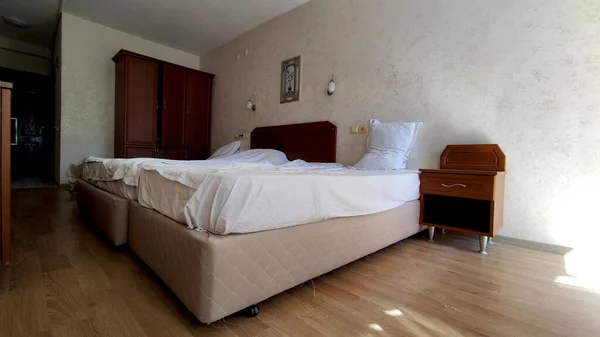 Cheap tourist hotel room with a view of the bed, sconces, cabinets, TV and wardrobe, hotel for one night, hotel rest, tourism and travel