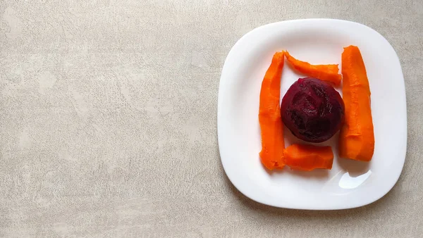 White plate with boiled carrots and beets, vegetarian breakfast on a white plate of boiled vegetables, top view, boiled carrots, boiled beets on a white textured table
