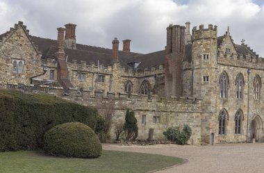 Mavi gökyüzüne karşı uzun bacaları ve taretleri olan retro gotik bir kalenin önü.