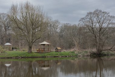 Nehrin karşı kıyısında, henüz yaprakları olmayan ağaç ve ahşap yapıları olan bir bahçeye bakıyorum.