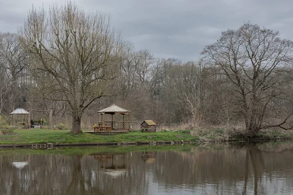 Nehrin karşı kıyısında, henüz yaprakları olmayan ağaç ve ahşap yapıları olan bir bahçeye bakıyorum.