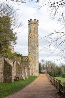 Looking along a stone pathway at a tall cream stone tower at the end of a wall to a castle 