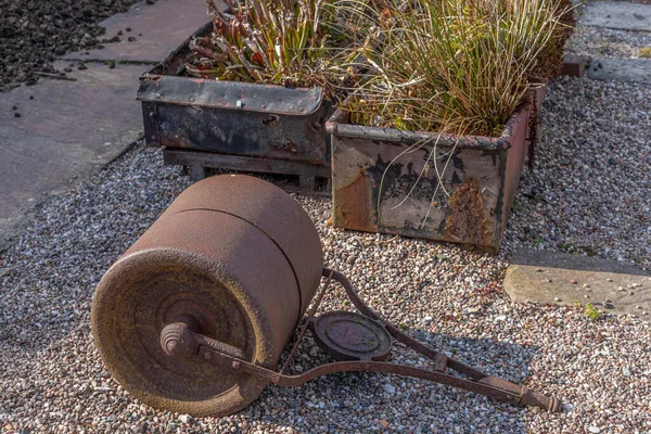 古く錆びた鋳鉄製の庭のローラーは 植物でいっぱいの金属製の箱の前に地面に横たわっています — ストック写真