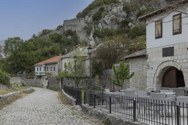 İşlenmiş demir çitler ve rattan sandalyelerle çevrili küçük bir Bosna köyünde kaldırımlı bir caddeye bakıyorum.