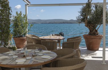 Kotor tatil beldesinde kıyı tarafında yemek yiyoruz. Ran mobilyaları ve yuvarlak ahşap masalarla denize bakıyoruz.