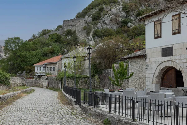 İşlenmiş demir çitler ve rattan sandalyelerle çevrili küçük bir Bosna köyünde kaldırımlı bir caddeye bakıyorum.