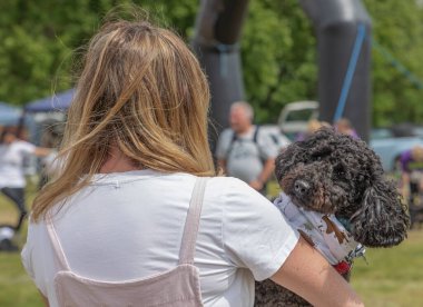 Sırtı kameraya dönük bir kadın kollarında siyah bir kaniş köpeği tutuyor. 